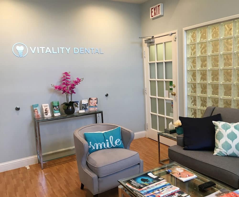 Modern dental office waiting room with blue accent wall, Vitality Dental signage, comfortable seating, and decorative elements.