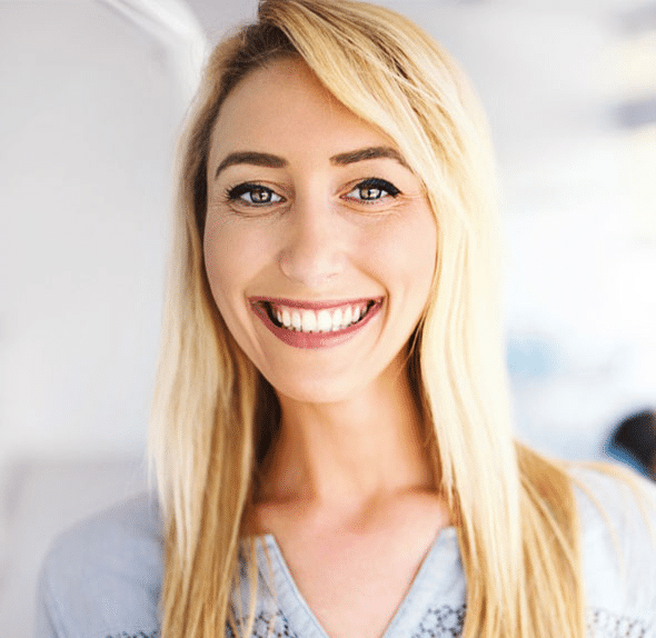 Smiling blonde woman in light blue shirt, professional headshot portrait indoors.
