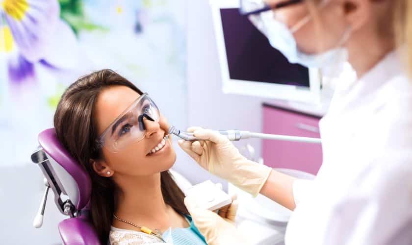 Dentist examining female patient's teeth in modern dental office with colorful background.